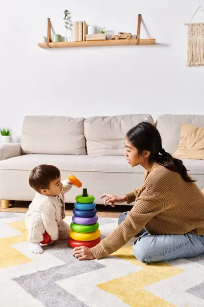 Una giovane madre asiatica gioca felicemente con il suo piccolo figlio sul pavimento nel loro accogliente soggiorno. — Foto stock