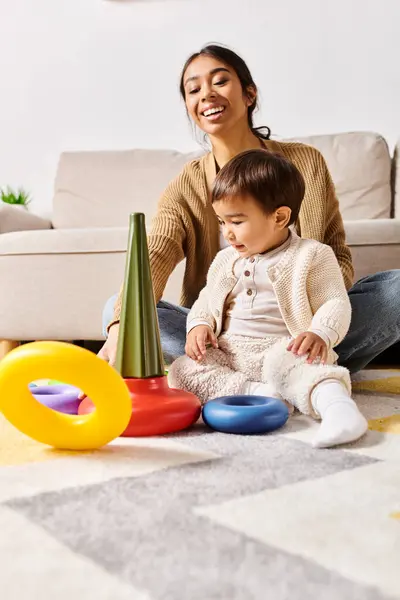 A young Asian mother sitting on the floor, happily playing with her little son in the living room of their home. — Stock Photo