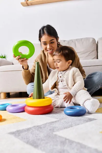 Una giovane madre asiatica interagisce gioiosamente con il suo piccolo figlio sul pavimento del loro soggiorno a casa. — Foto stock