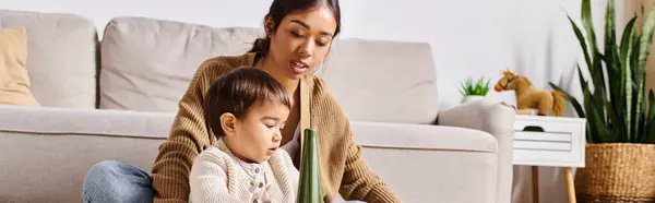 A young Asian mother sits on the floor, embracing her child in a warm and loving moment at home in the living room. — Stock Photo