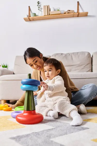 A young Asian mother joyfully interacts with her little son, playing together on the floor in their cozy living room. — Stock Photo