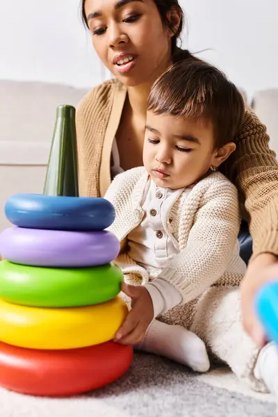 Una joven madre asiática y su pequeño hijo jugando felizmente con una pila de juguetes en la sala de estar. - foto de stock