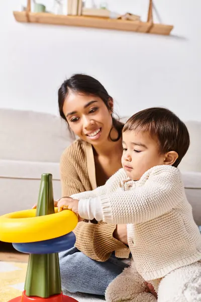 A young Asian mother joyfully playing with her little son on the floor in their cozy living room. — Stock Photo