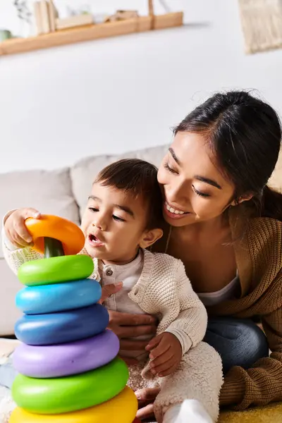 A young Asian mother joyfully interacts with her little kid as they play together on the floor in their cozy living room. — Stock Photo