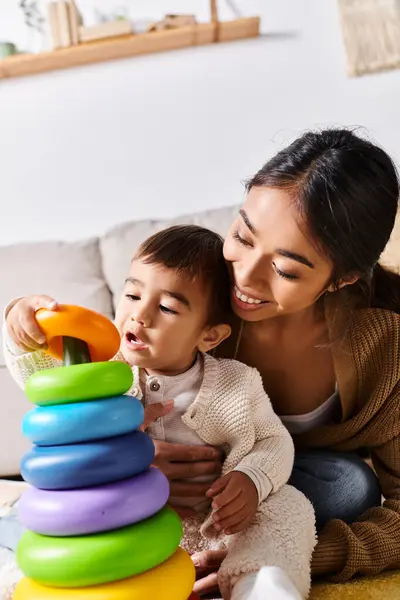 Una giovane madre asiatica interagisce gioiosamente con il suo bambino mentre giocano insieme sul pavimento nel loro accogliente soggiorno. — Foto stock