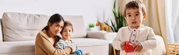 A young Asian mother and her two little sons sit closely together on a cozy couch in their living room. — Stock Photo