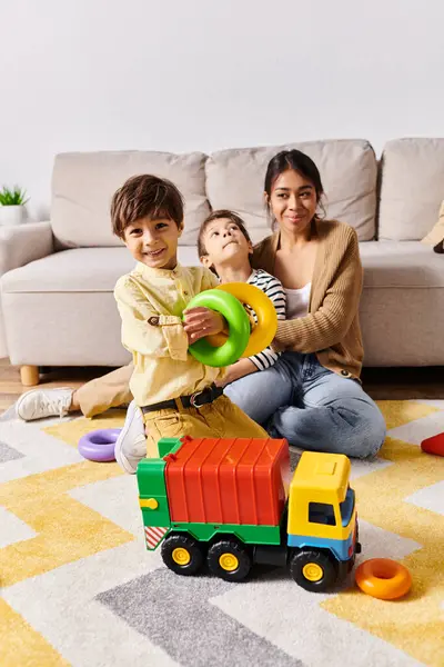 Une jeune mère asiatique et ses deux petits fils jouent joyeusement avec un camion jouet dans leur salon. — Photo de stock