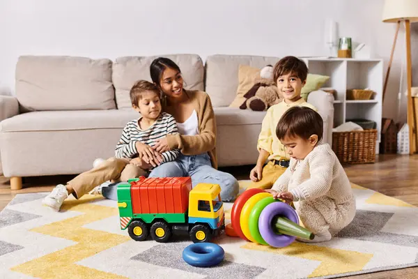 Una joven madre asiática y sus hijos pequeños están jugando felizmente con juguetes en su sala de estar. - foto de stock