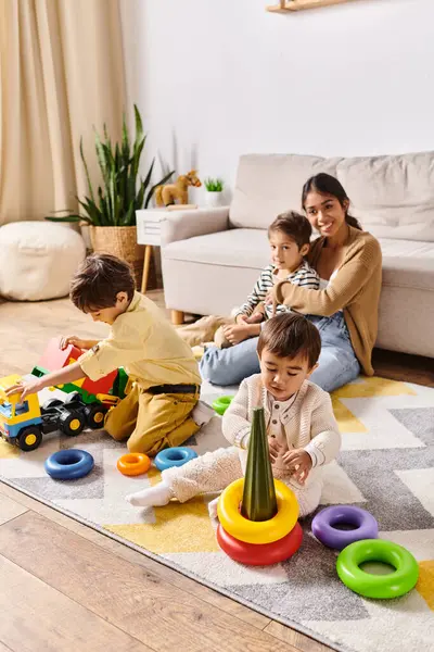A young Asian mother watches as her little sons play with colorful toys in a warm, inviting living room. — Stock Photo