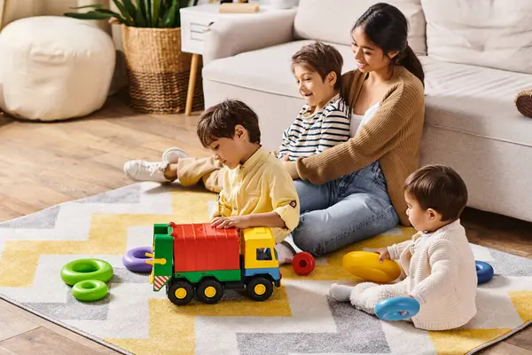 Una joven madre asiática se sienta en el suelo, jugando alegremente con sus hijos pequeños en la acogedora sala de estar de su casa. - foto de stock