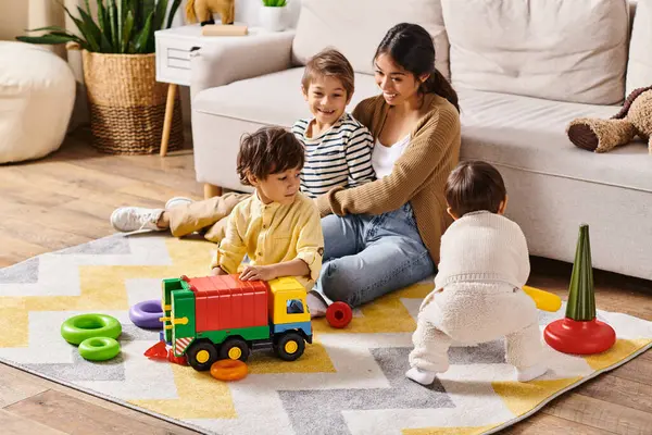A young Asian mother joyfully sits on the floor, playing with her two little sons in their cozy living room. — Stock Photo