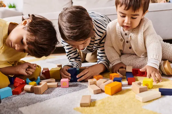Tre bambini piccoli, probabilmente fratelli, si impegnano in giochi fantasiosi mentre costruiscono con blocchi di legno sul pavimento del soggiorno.. — Foto stock