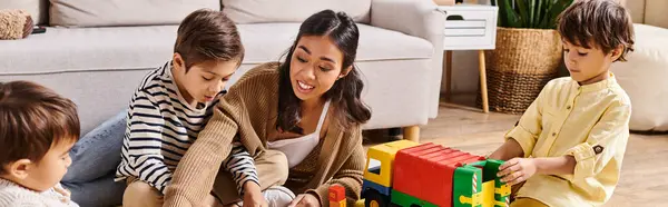 Jovem mãe asiática absorvida em atividades lúdicas com seus filhinhos no ambiente acolhedor da sala de estar. — Fotografia de Stock