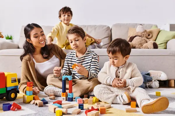 Un grupo de niños, guiados por su joven madre asiática, juegan con entusiasmo, apilan bloques y se sumergen en un juego imaginativo. - foto de stock