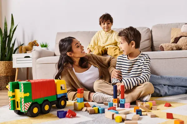 A young Asian mother sitting on the floor, joyfully playing with her little sons in the cozy living room of their home. — Stock Photo