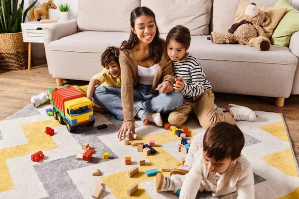 Una giovane madre asiatica e i suoi piccoli figli costruiscono gioiosamente strutture con blocchi colorati sul pavimento del loro soggiorno. — Foto stock