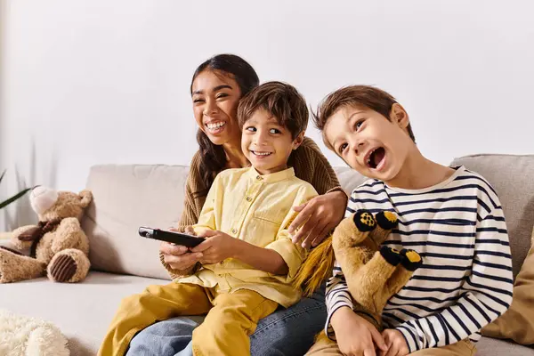 Children, along with their Asian mother, relax on a couch holding remote controls in a cozy living room setting. — Stock Photo