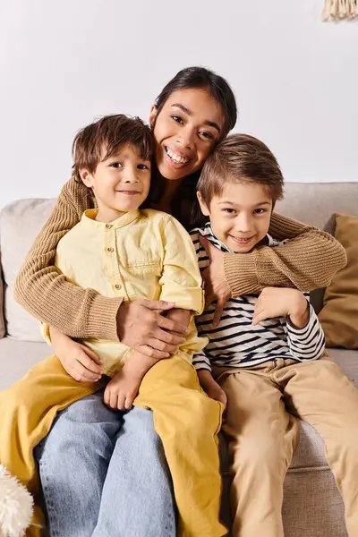 A young Asian mother sits on a couch, surrounded by her two energetic little sons, in their cozy living room at home. — Stock Photo