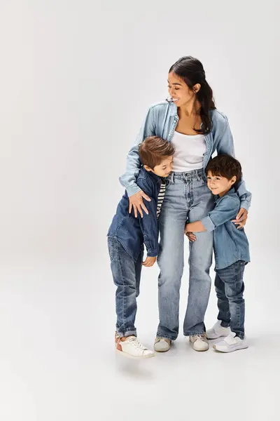 Eine junge asiatische Mutter und ihre kleinen Söhne, alle in Jeanskleidung, posieren in einem grauen Studio für ein Foto. — Stockfoto
