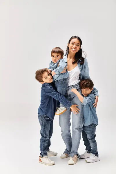Una giovane madre asiatica posa con i suoi piccoli figli, tutti vestiti in denim, catturando un momento commovente in uno studio grigio. — Foto stock