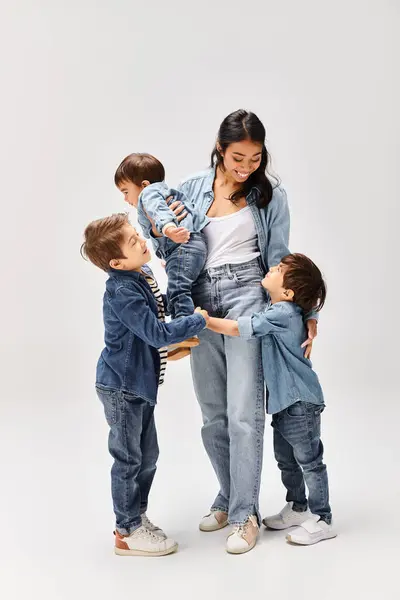 Giovane madre asiatica ei suoi tre figli, tutti vestiti in denim, stare uniti di fronte a un fondo bianco pianura. — Foto stock