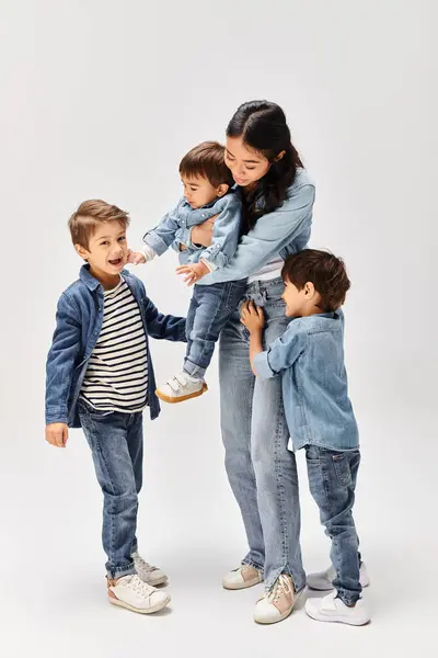 Un groupe d'enfants, dont une jeune mère asiatique et ses petits fils, debout l'un à côté de l'autre dans un studio gris, tous vêtus de denim. — Photo de stock