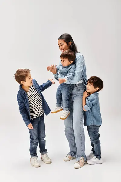 A young Asian mother and her little sons, dressed in denim, having a playful and joyful time together in a grey studio. — Stock Photo