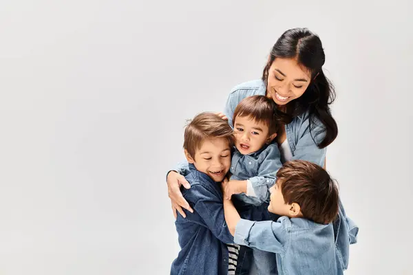 Una giovane madre asiatica abbraccia i suoi due piccoli figli, tutti vestiti in denim, creando un commovente momento di amore e connessione. — Foto stock