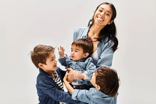 Una giovane madre asiatica e i suoi piccoli figli, tutti vestiti di denim, che si divertono e giocano insieme in uno studio grigio. — Foto stock