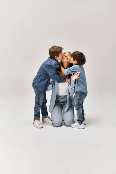 Una madre con i suoi figli, che si abbracciano in uno studio grigio mentre tutti indossano abiti in denim. — Foto stock