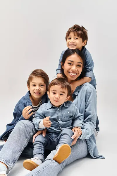 Una giovane madre asiatica e i suoi piccoli figli si impilano scherzosamente l'uno sopra l'altro, indossando tutti abiti in denim in uno studio grigio. — Foto stock
