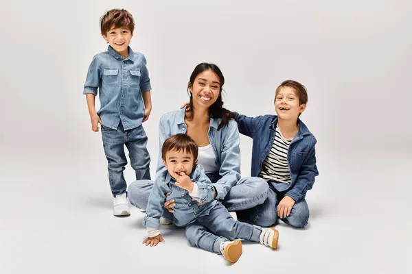 Una joven madre asiática y sus hijos pequeños con ropa de mezclilla posando juntos en un elegante estudio gris. - foto de stock