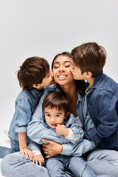 Молодая азиатская мать сидит на земле со своими детьми, все одеты в джинсовую одежду, создавая тесную связь. — стоковое фото