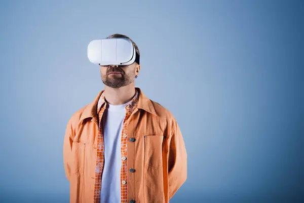 Un uomo con una camicia arancione esplora il metaverso in una cuffia bianca di realtà virtuale all'interno di uno studio. — Foto stock