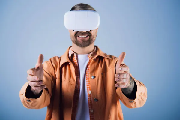 Un uomo in camicia arancione sperimenta la realtà virtuale attraverso un auricolare in un ambiente hi-tech da studio. — Foto stock