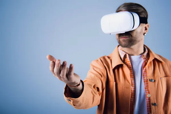 Un uomo con una camicia arancione è immerso nel metaverso mentre sperimenta la realtà virtuale in un ambiente da studio. — Foto stock