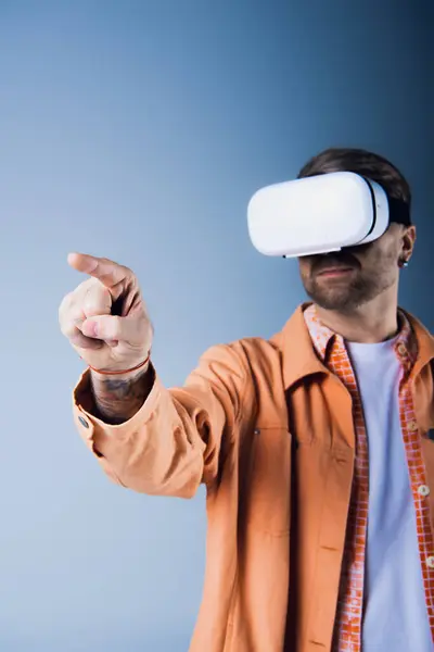 Un hombre con una chaqueta naranja apunta mientras usa un casco VR en un ambiente de estudio. - foto de stock