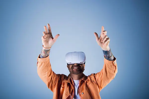 A man in an orange jacket stands, wearing a white vr headset, against a vivid backdrop. — Stock Photo
