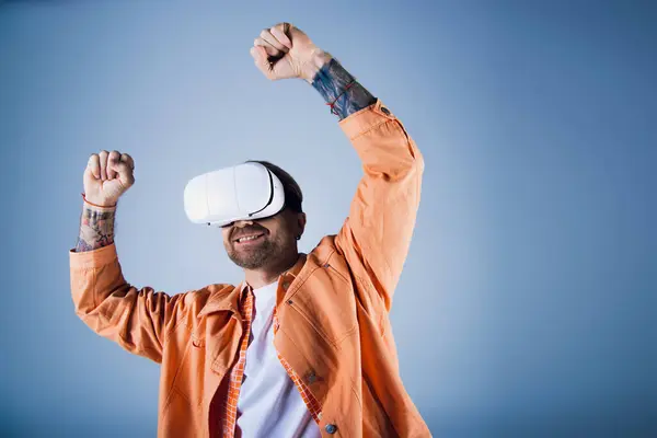 Un uomo con una camicia arancione scava nel Metaverse attraverso una cuffia di realtà virtuale in un ambiente da studio. — Foto stock