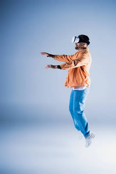 A man in a VR headset jumps energetically in a studio setting, showcasing his acrobatic skills while wearing a stylish hat. — Stock Photo