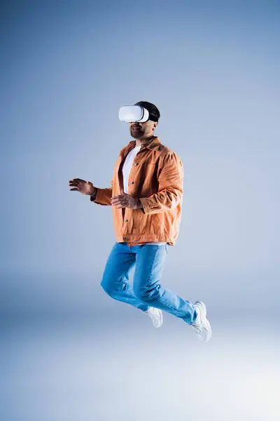 Un hombre con un sombrero salta en el aire dentro de un entorno de estudio mientras usa un casco VR para la exploración de metáforas. - foto de stock