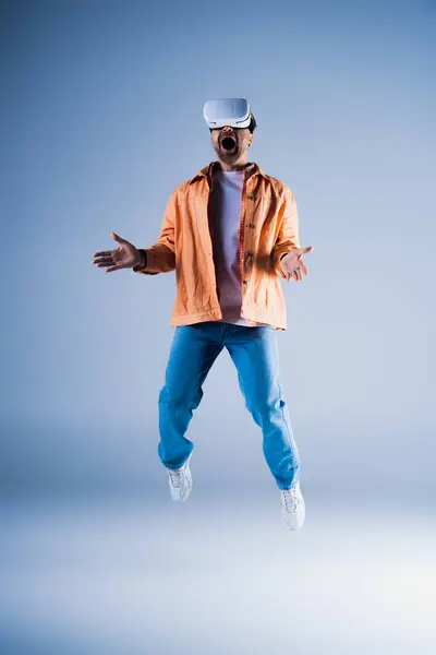 A man in a vibrant orange jacket is caught mid-air, showcasing his energetic leap in a studio setting. — Stock Photo