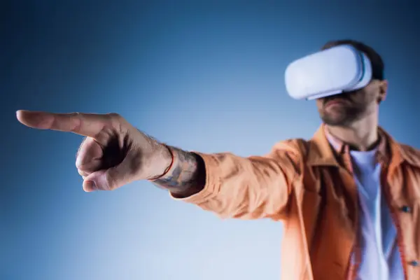 Un homme portant un chapeau pointe vers quelque chose alors qu'il est dans un casque de réalité virtuelle dans un décor de studio. — Photo de stock