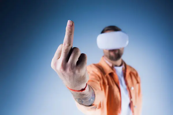Ein Mann mit verbundenen Augen und einem VR-Headset zeigt selbstbewusst auf ein unsichtbares Ziel im Studio, Mittelfinger — Stockfoto