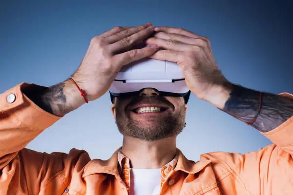 Um homem vestindo uma camisa laranja em um estúdio, imerso em uma experiência de realidade virtual. — Fotografia de Stock