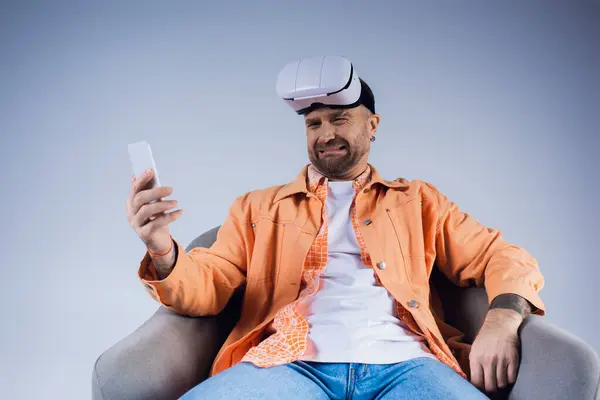 Un homme plongé dans le monde virtuel, assis dans une chaise tenant un téléphone portable dans un décor de studio. — Photo de stock