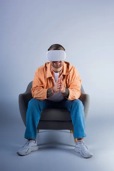 Un hombre en una silla con una venda en los ojos, perdido en el mundo virtual con auriculares VR, en un estudio. - foto de stock