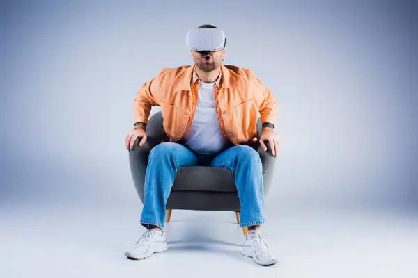 Un homme plongé dans la métaverse avec un casque de réalité virtuelle, assis dans une chaise dans un environnement studio. — Photo de stock