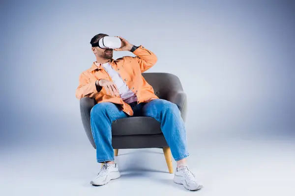 Um homem senta-se confortavelmente em uma cadeira, vestindo um fone de ouvido VR, perdido em pensamento em um estúdio. — Fotografia de Stock