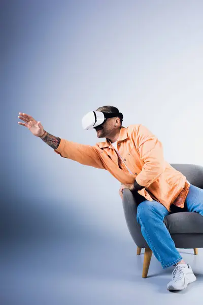 Un hombre con auriculares VR se sienta en una silla con la mano levantada, inmerso en un mundo virtual - foto de stock